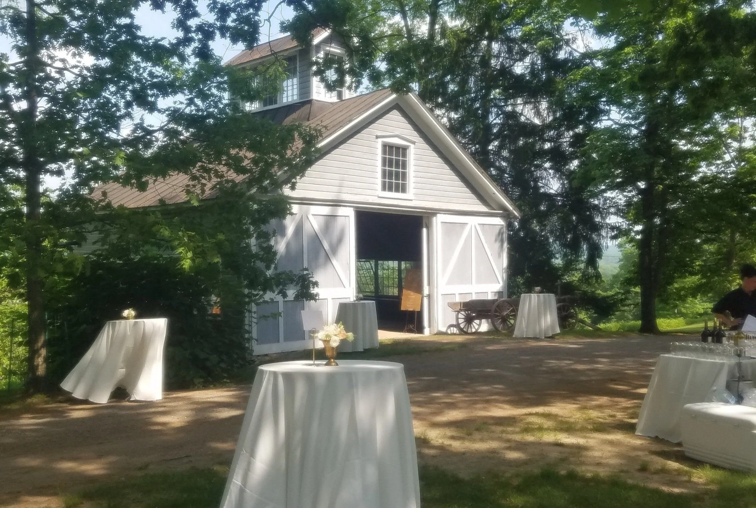 A white barn transformed into a picturesque wedding venue with tables and chairs set up in front of it for cocktail hour