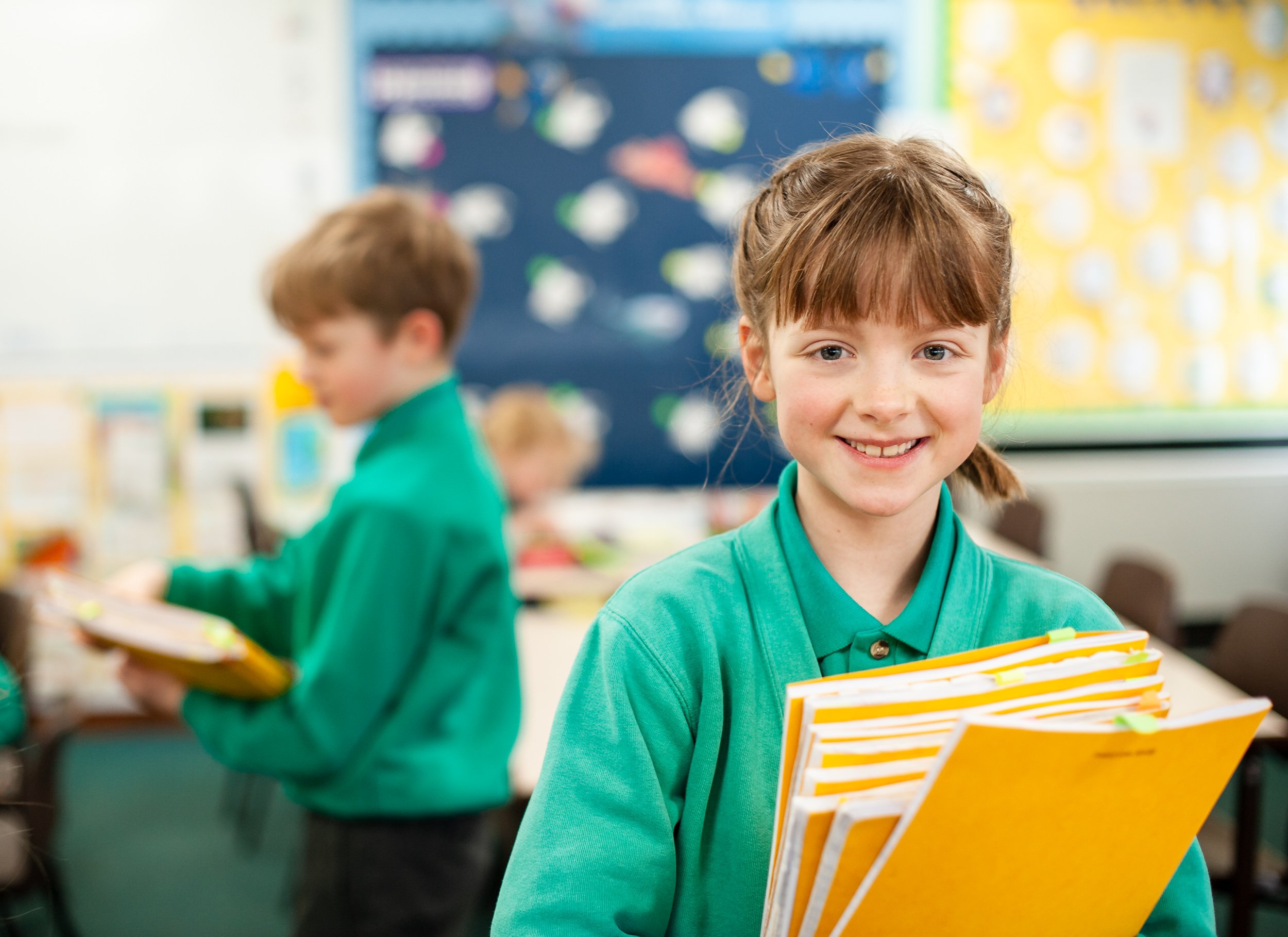 girl carrying yellow school books in classroom, Manchester