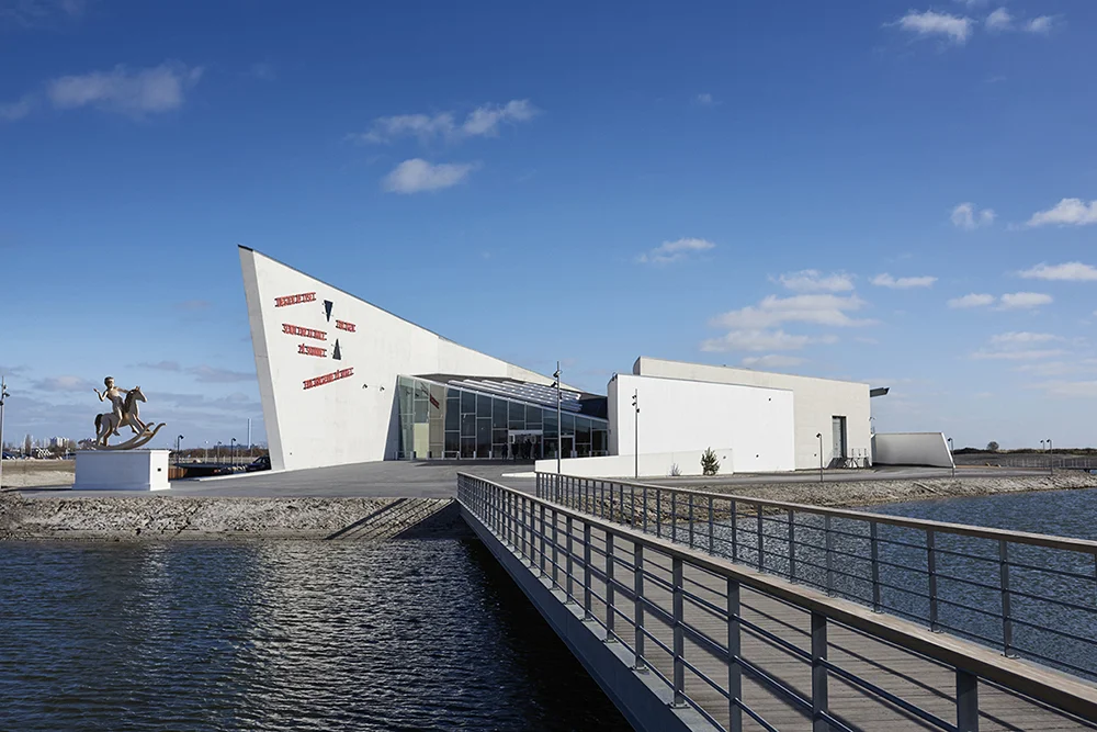 Arken Museum for Moderne Kunst "ARKEN Museum for Moderne Kunst ligger stor og monumental midt i det menneskeskabte landskab, Køge Bugt Strandpark, syd for København. ARKEN har en af Skandinaviens fineste samlinger af samtidskunst og museets maritime arkitektur med den spidse stævn, der majestætisk stikker frem i terrænet, har vundet anerkendelse i både ind- og udland." Adresse: Skovvej 100, 2635 Ishøj. Links: Arken.dk | Læs mere på idoart.dk Foto: Henrik Jauert.