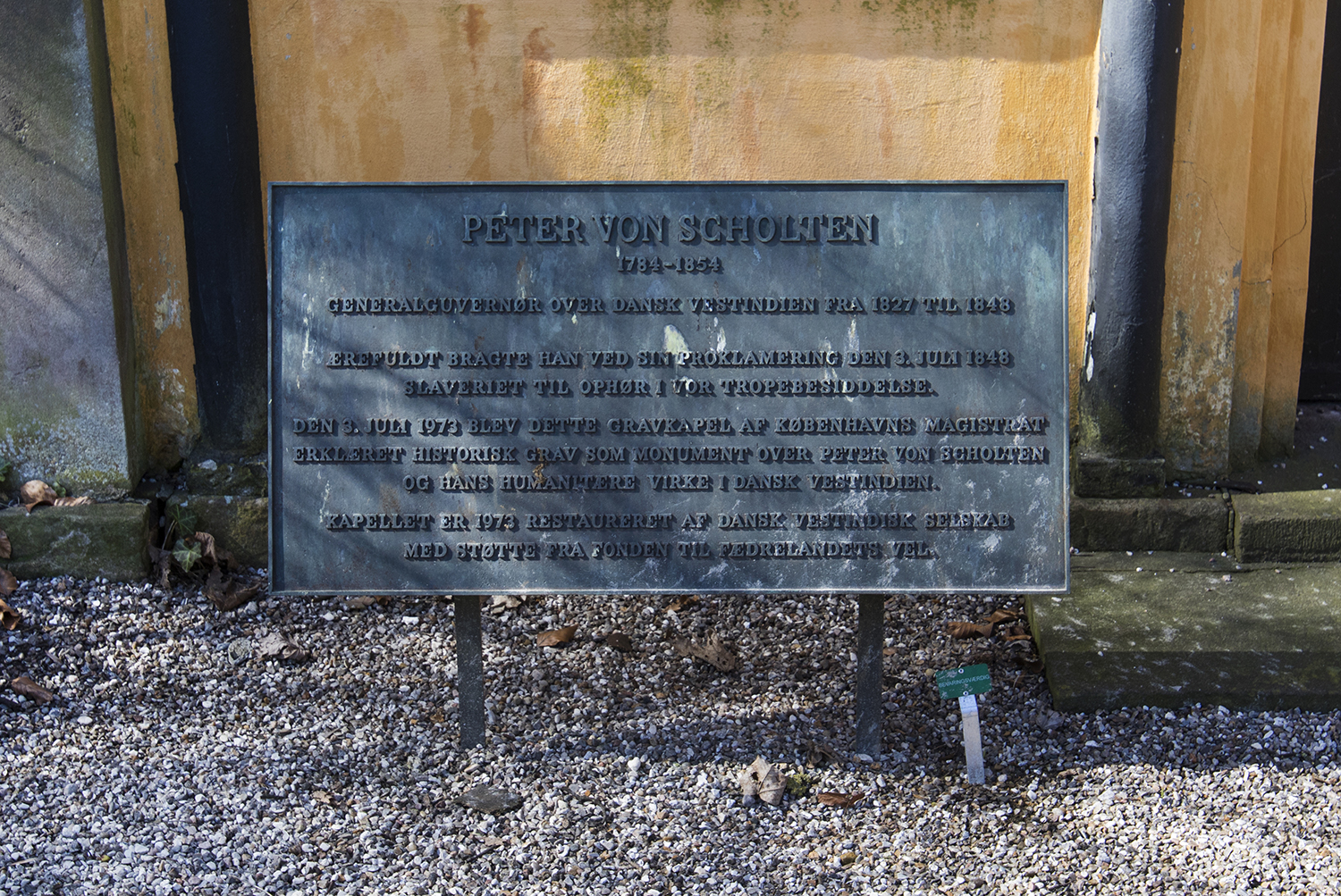 "Peter von Scholten, 1784 - 1854. Generalguvernør over Dansk vestindien fra 1827 til 1848. Ærefuldt bragte han ved sin proklamering den 3. juli 1848 slaveriet til ophør i vor tropebesiddelse. Den 3. juli 1973 blev dette gravkapel af Københavns Magistrat erklæret historisk grav som monument over Peter von Scholten og hans humanitære virke i Dansk Vestindien. Kapellet er 1973 restaureret af Dansk Vestindisk Selskab med støtte fra fonden til fædrelandets vel." står der på mindetavlen foran von Scholtens mausoleum på Assistens Kirkegåden. I Danmark er von Scholten blevet hyldet som helt, men på Jomfruøerne er historien en anden. Photo © I DO ART Agency.