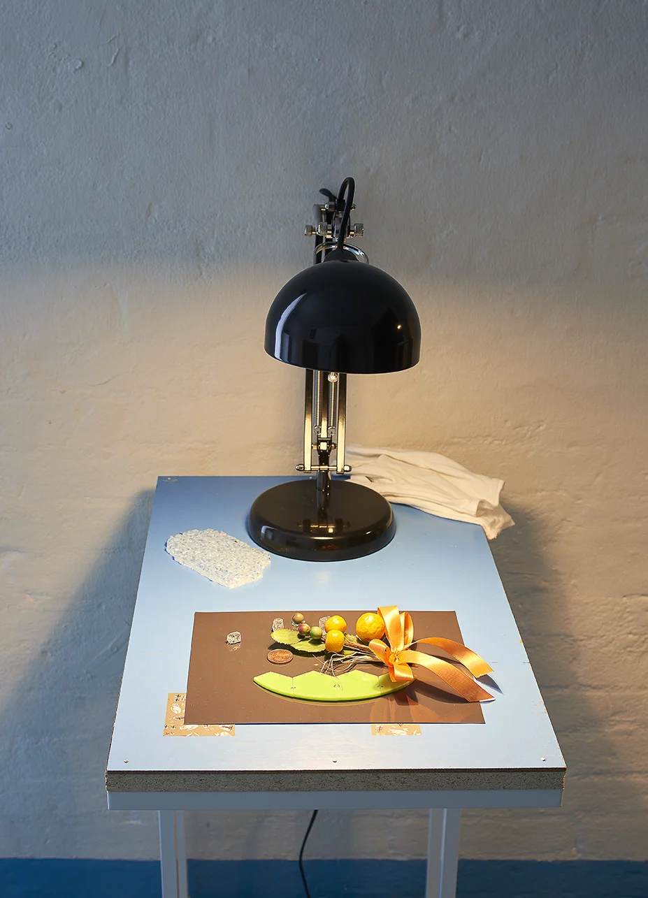 Kah Bee Chow âUden titel,â 2019 (chipboard, lamp, laptop table, coin, grass, ribbon, laser-cut plexiglass, wash tape, silicone, nails, photo paper). Foto: Kirstine Mengel.