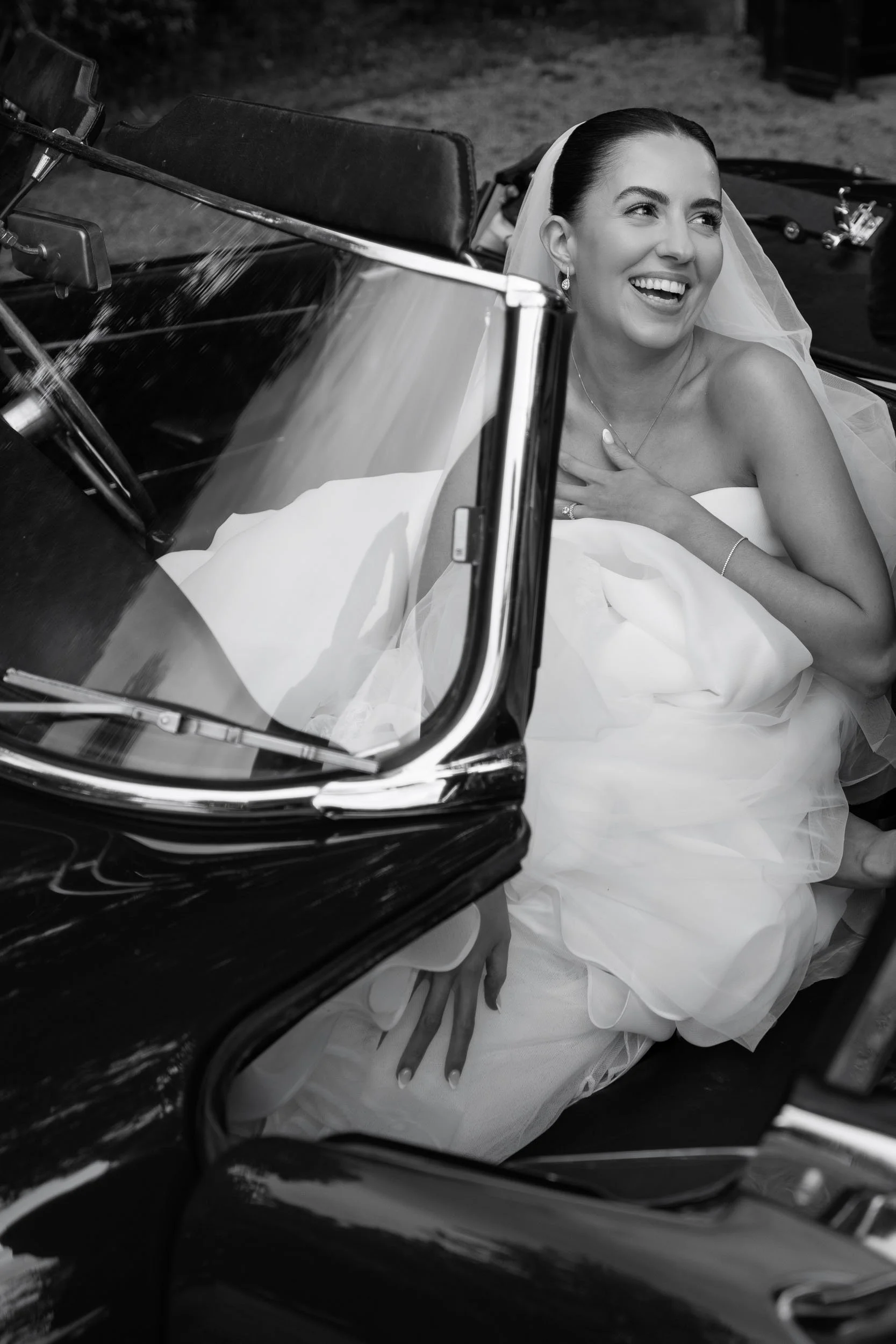 Joyful black-and-white portrait of a laughing bride sitting in a vintage wedding car at Middleton Lodge Estate, North Yorkshire.