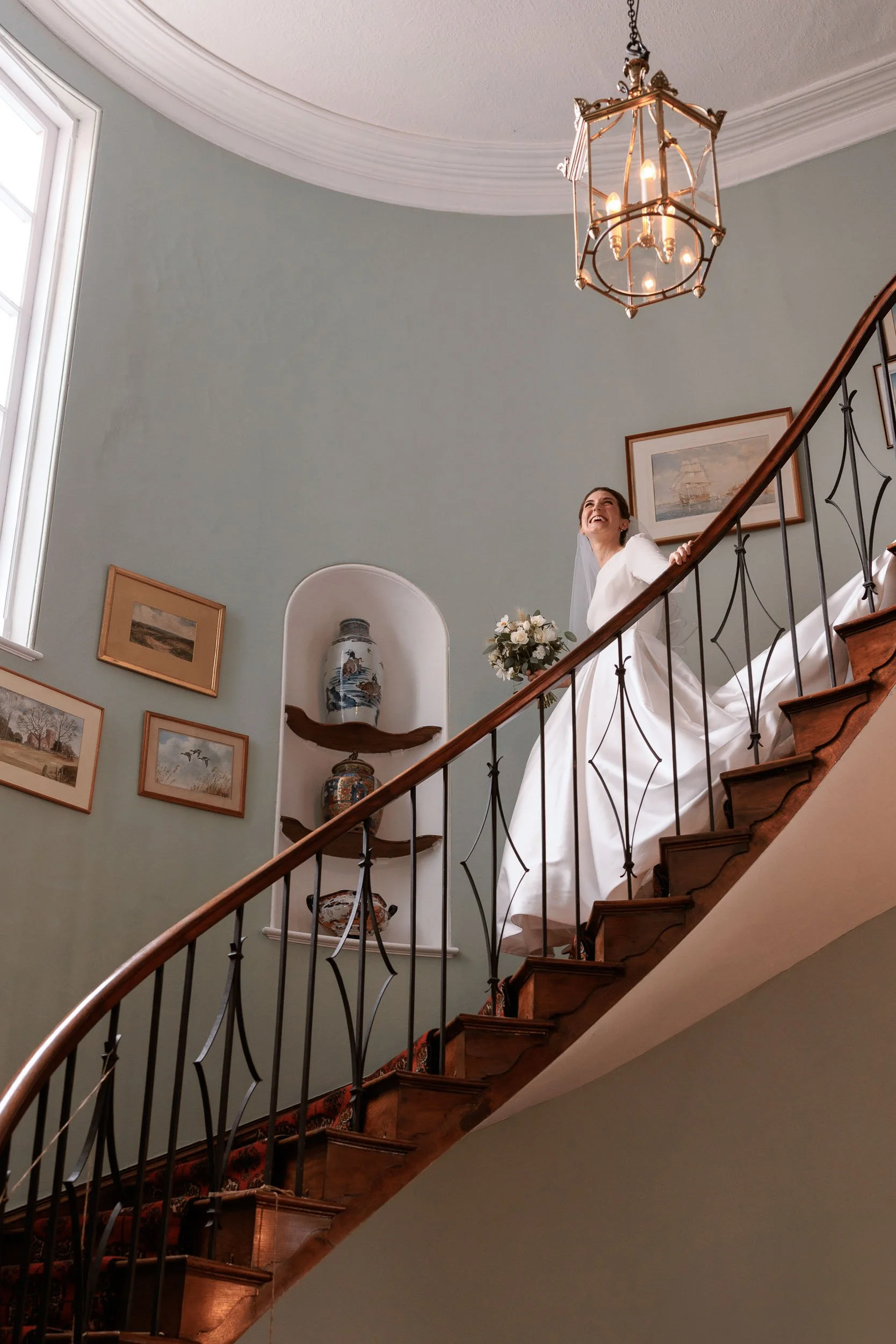 Bride descending the staircase at Homme House, an elegant historic country house in Herefordshire.