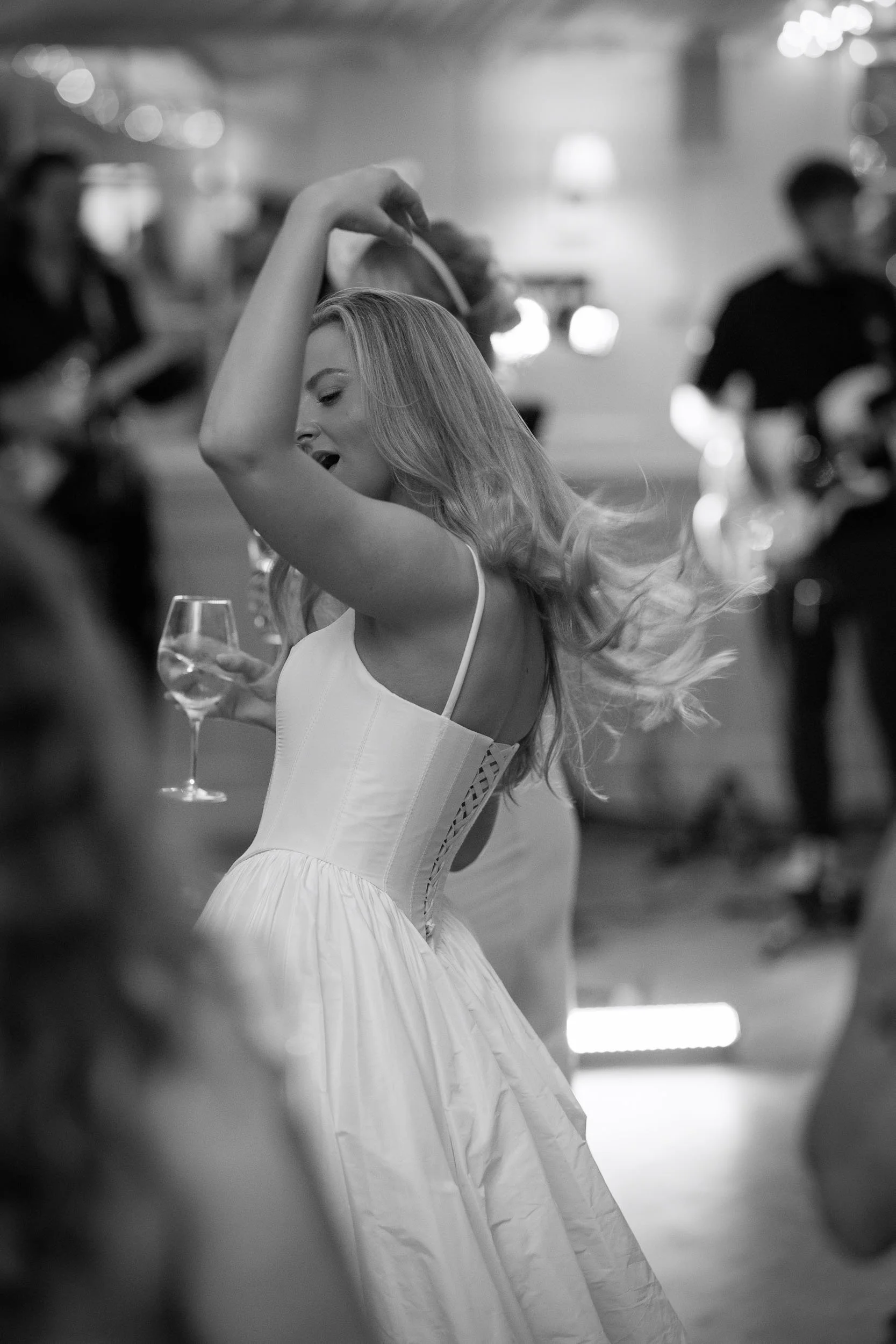 Black-and-white candid photograph of a wedding guest dancing with a glass of wine during the evening celebrations at Middleton Lodge Estate, North Yorkshire.