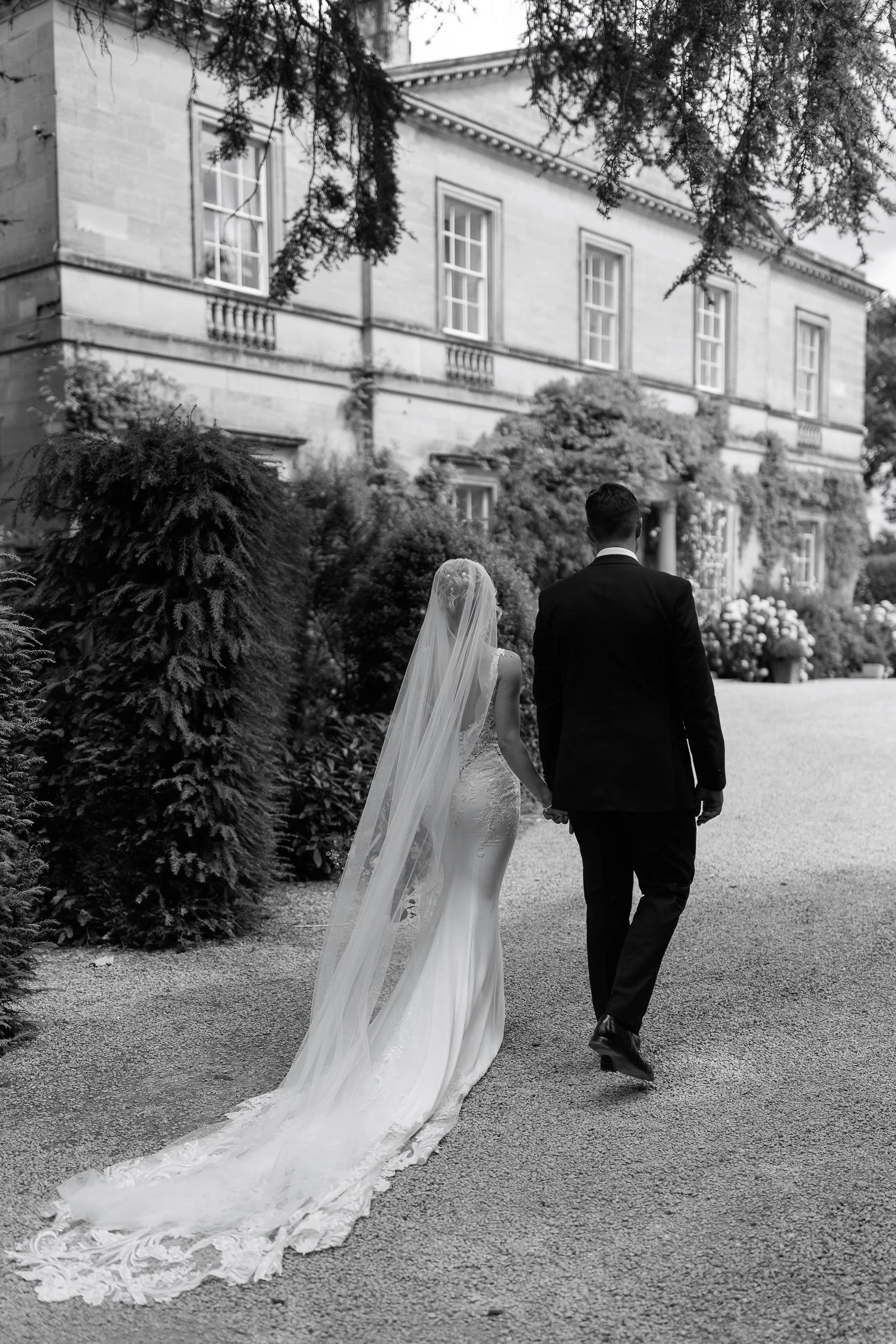 Black and white portrait of newlyweds walking beside the Main House at Middleton Lodge.