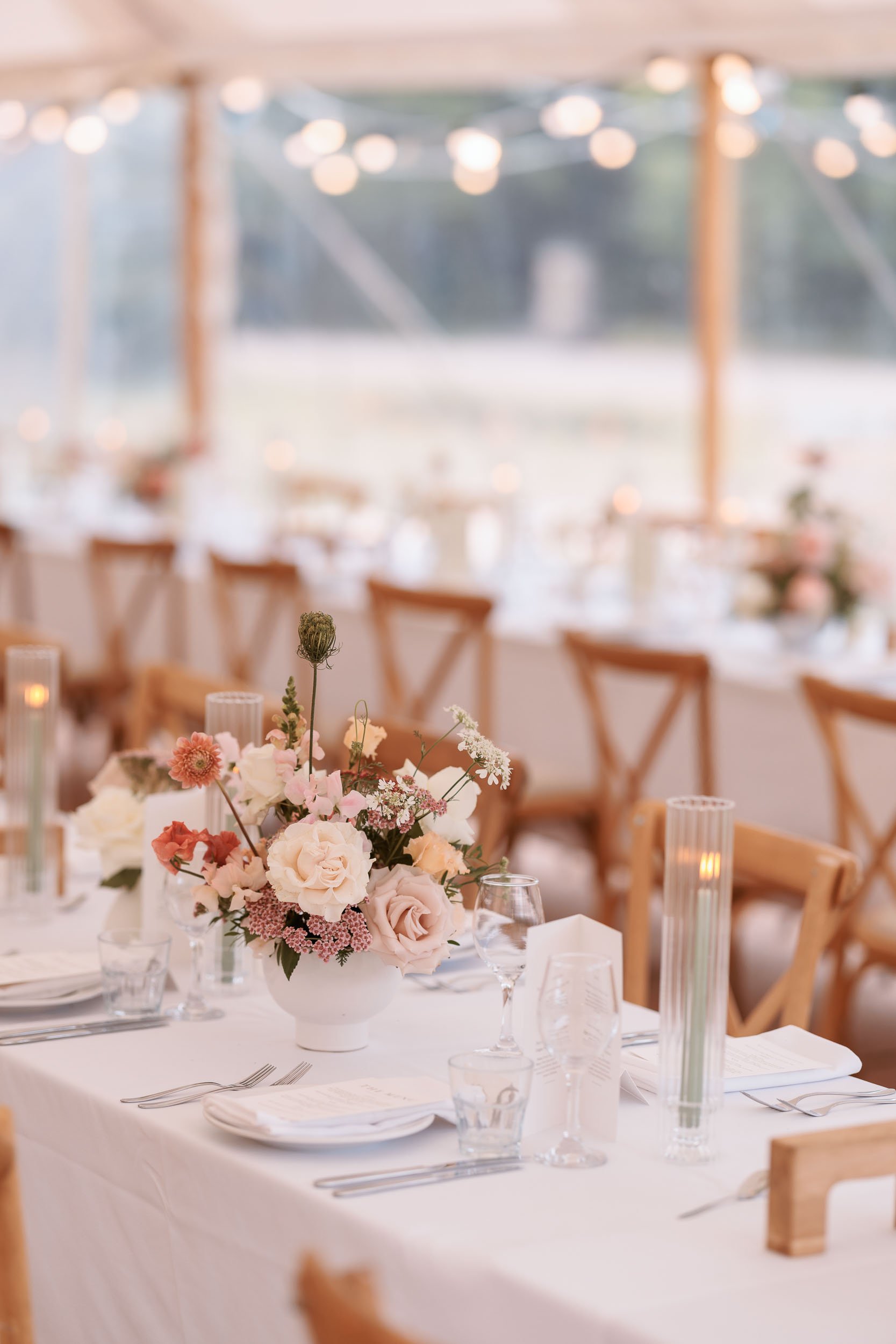 Elegant wedding reception table at Newburgh Priory, with pastel floral arrangements, candles and wooden chairs inside a beautifully decorated marquee.