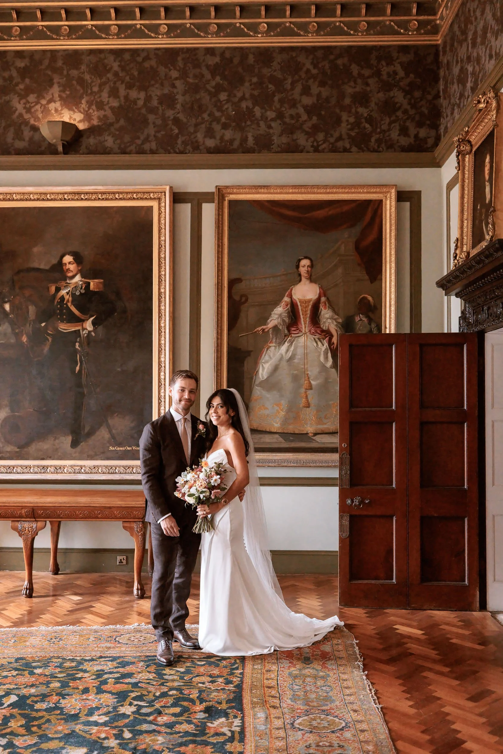 Bride and groom photographed inside Newburgh Priory, surrounded by historic oil paintings, ornate wooden details and period furnishings.