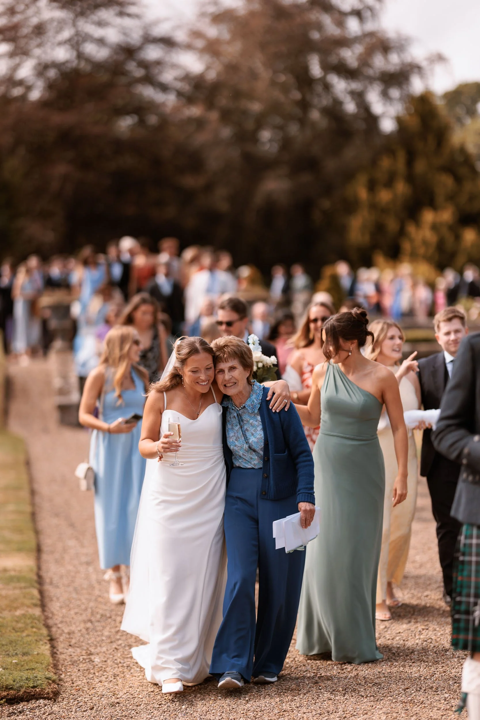 Bride walking arm in arm with a guest through the grounds of Egton Manor, surrounded by family and friends enjoying the wedding celebrations.