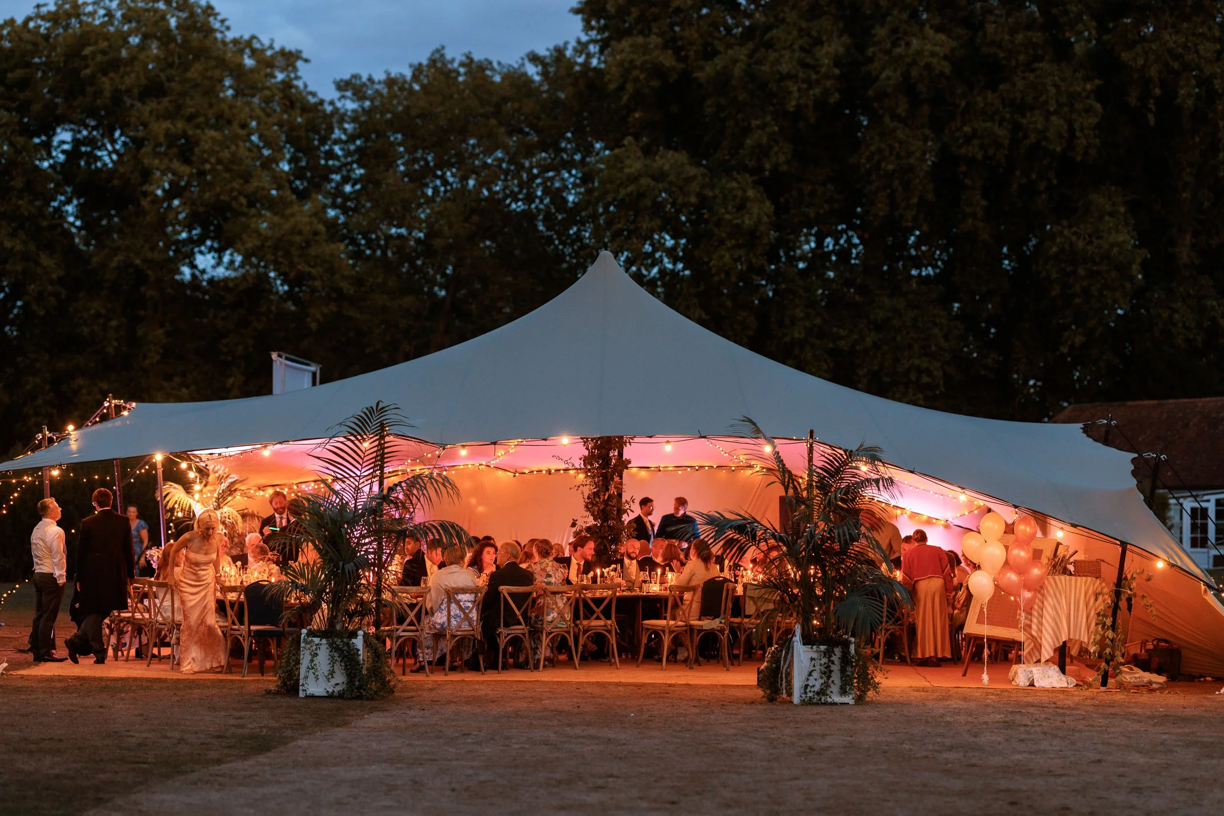 Evening wedding reception beneath a marquee surrounded by trees in the grounds of Windsor Castle