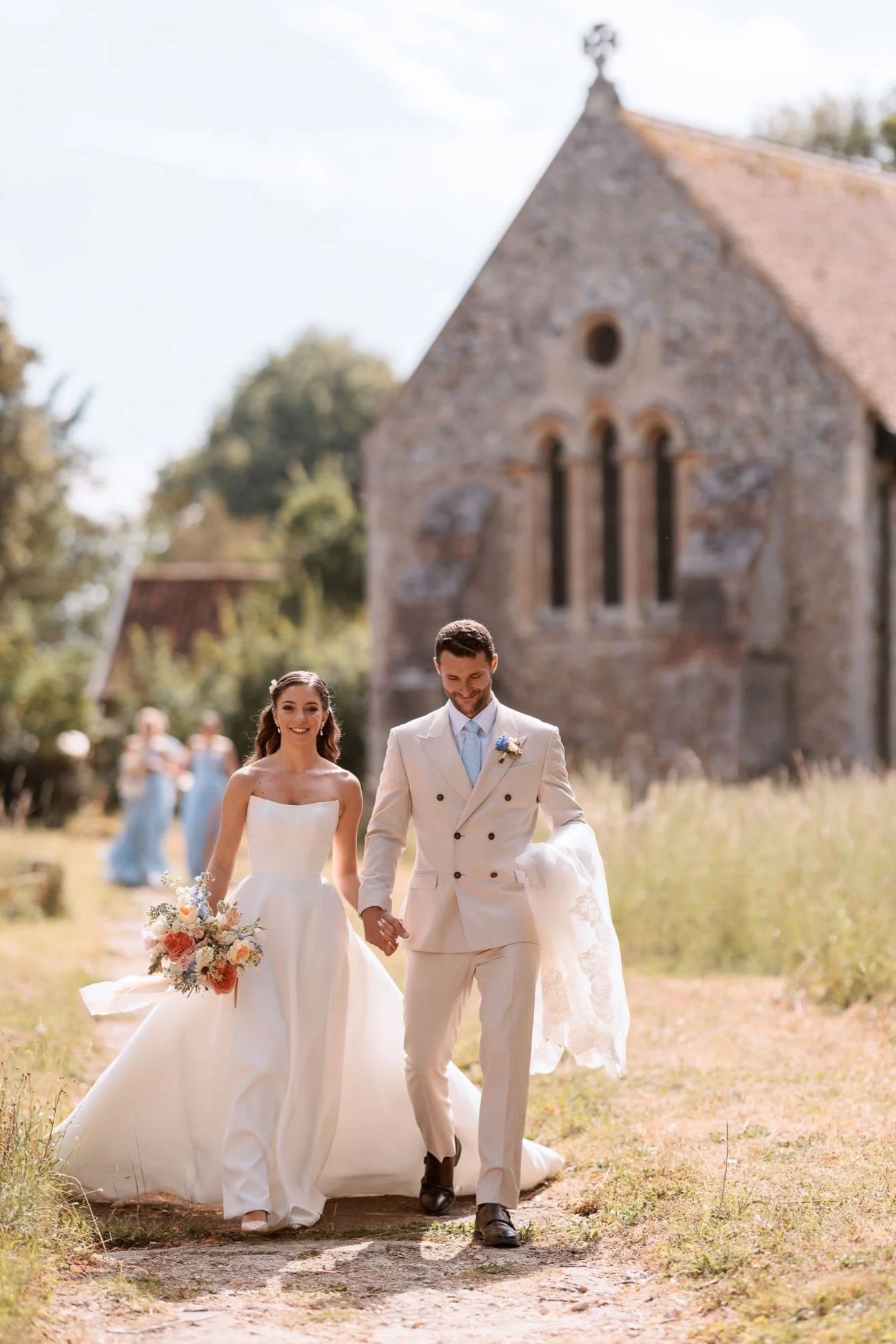 Newly married couple walking together outside a historic English church during a summer wedding photographed by Neil Jackson.