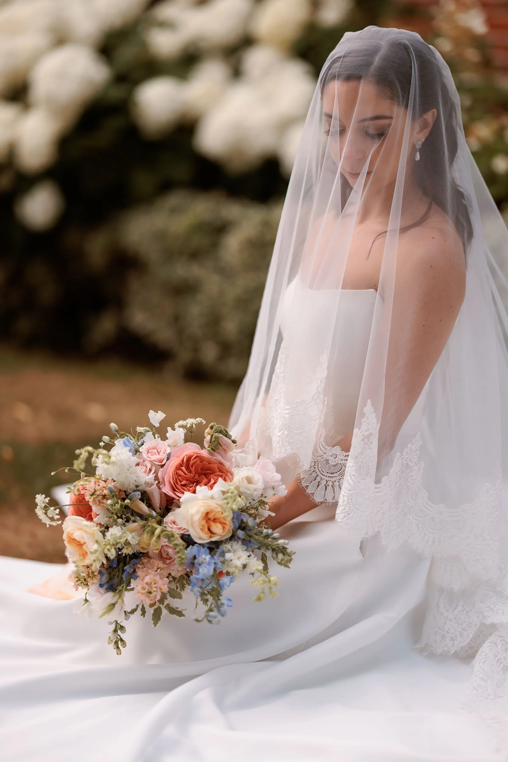 Bride wearing a lace-edged veil and holding a colourful summer bouquet in an editorial wedding portrait.