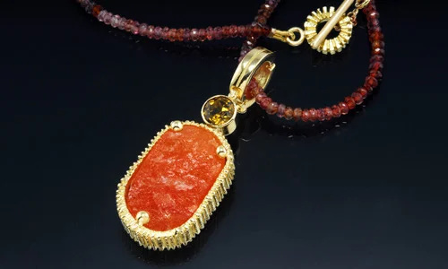   Custom pendant in 18K yellow gold with natural surface sunstone and round faceted mali garnet. Displayed on 4mm sapphire beads.  