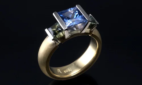  Engagement ring in 18K yellow and white gold with tanzanite and grey-green tourmaline. Band width approximately 0.3" 
 Please feel free to contact us for stone options  