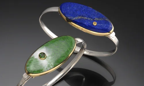   Cuff bracelet made of sterling silver and 18K yellow gold. Left cuff with polished inlay of maw-sit-sit and accented by a 4.5mm green tourmaline. Right cuff with natural surface lapis and accented by a 2.5mm yellow sapphire. Inlay measures approxim