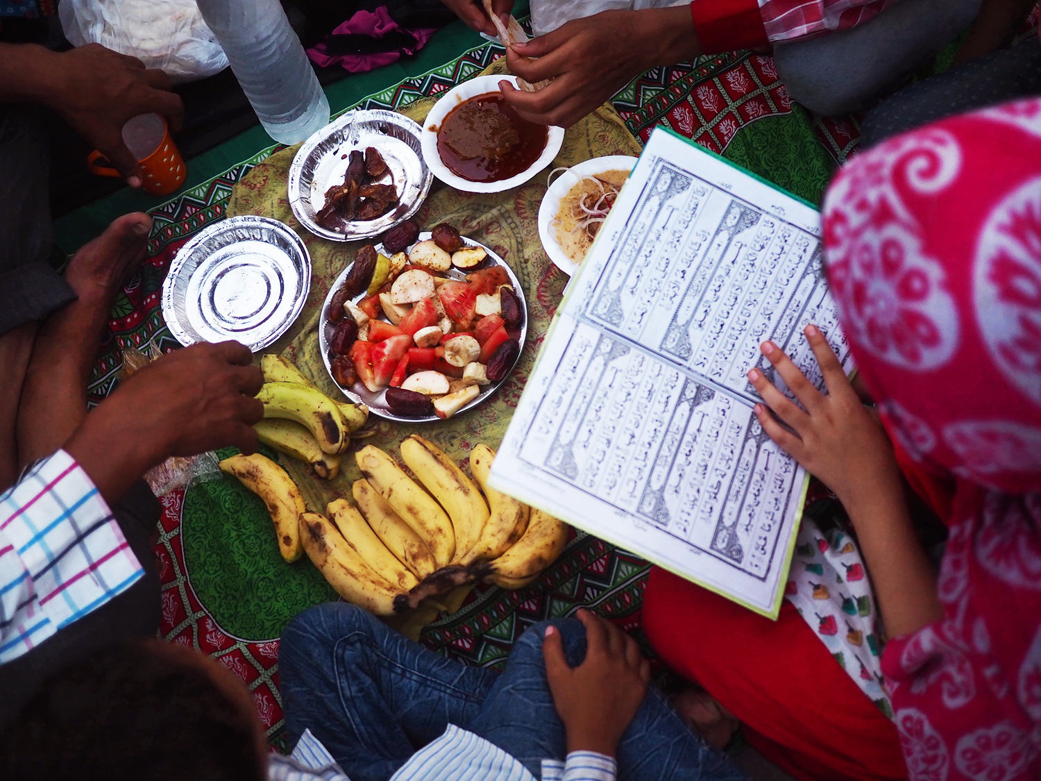 A young girl studies the Quran as her family prepares for the breaking of fast.