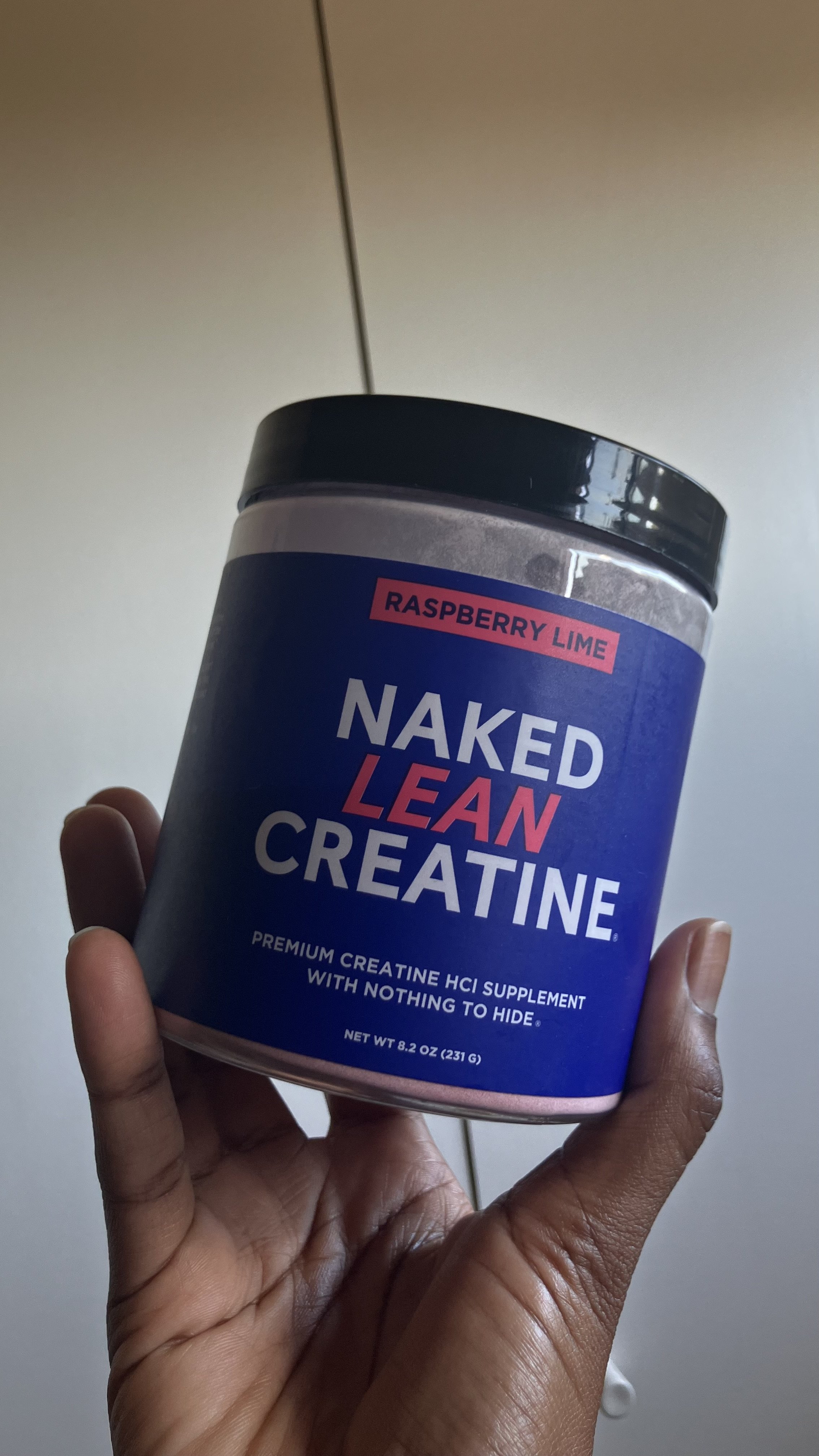 a hand holding a container of naked nutrition lean creatine
