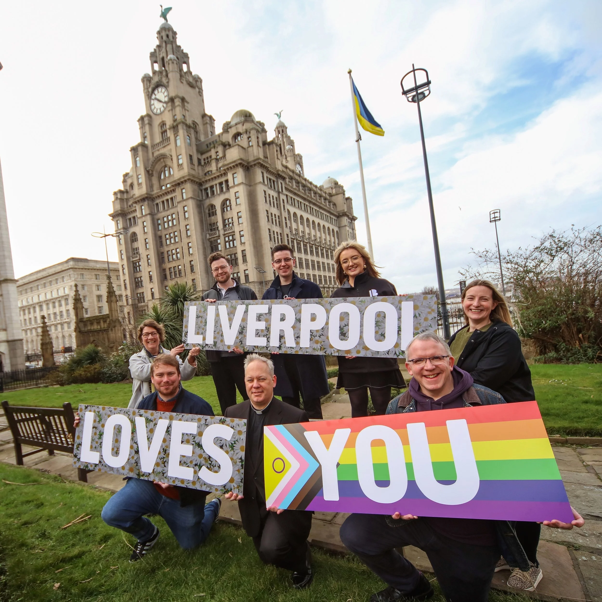 Members of the ‘Liverpool Loves You’ partnership hold signs saying ‘Liverpool Loves You’ in front of the city’s iconic Liver Building. PHOTO: Matt Goodfellow