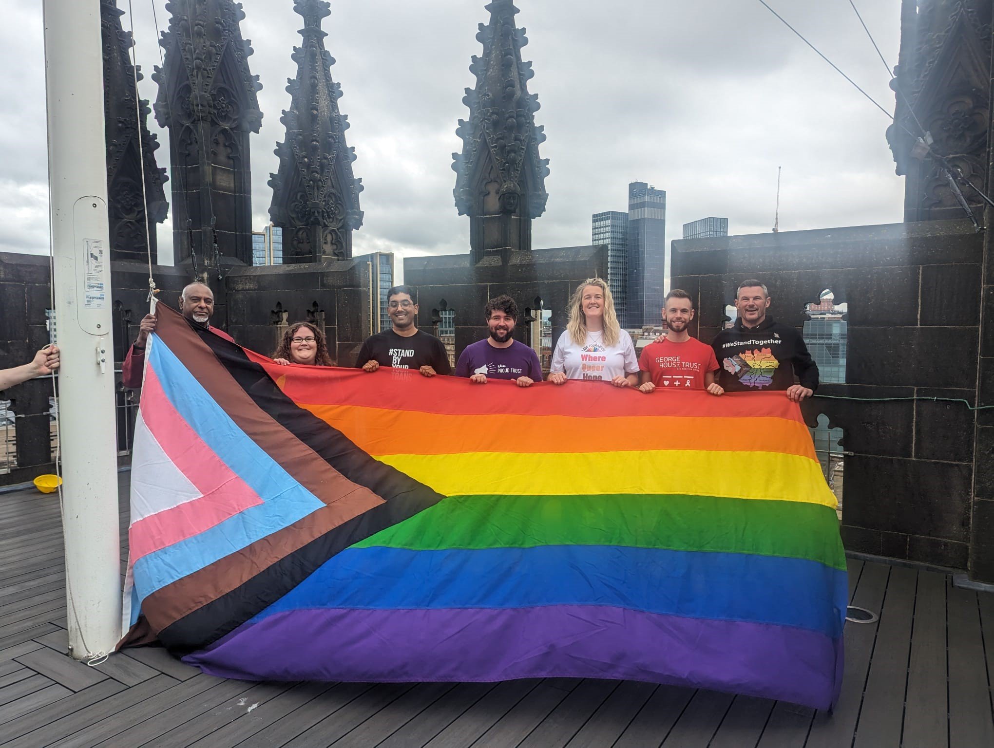  Team members at Manchester Cathedral standing on the roof of the church holding the Pride Progress flag, preparing to fly it during Pride weekend last month. 