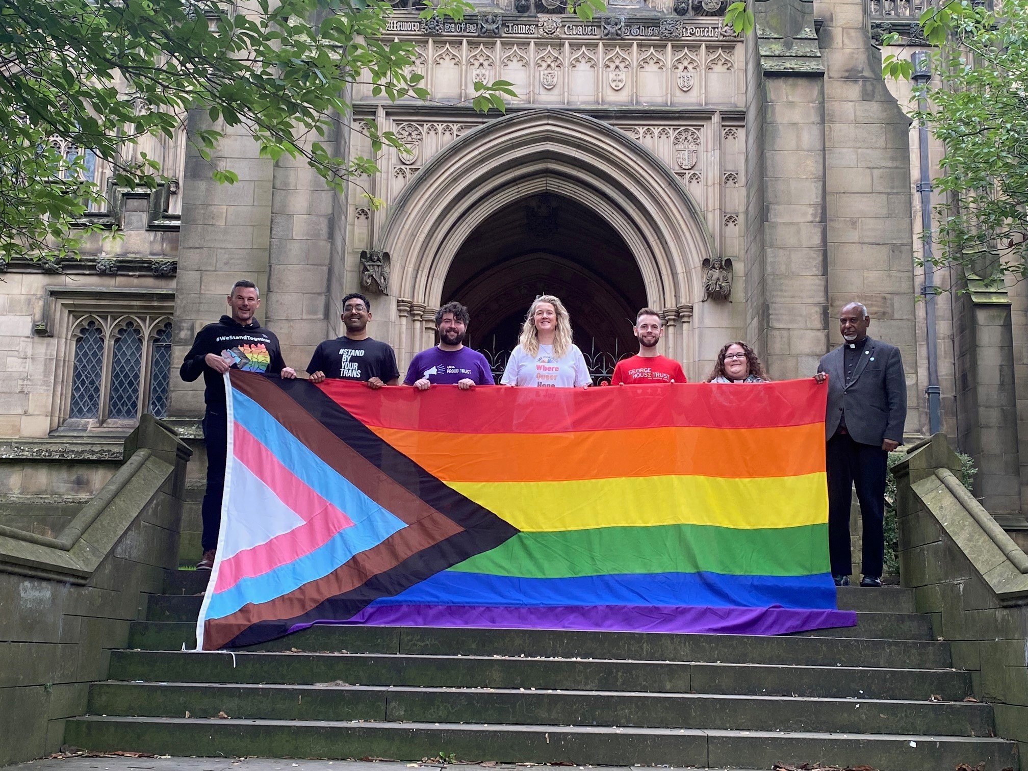  Team members at Manchester Cathedral standing on the steps up to the church holding the Pride Progress flag, preparing to fly it during Pride weekend last month. 
