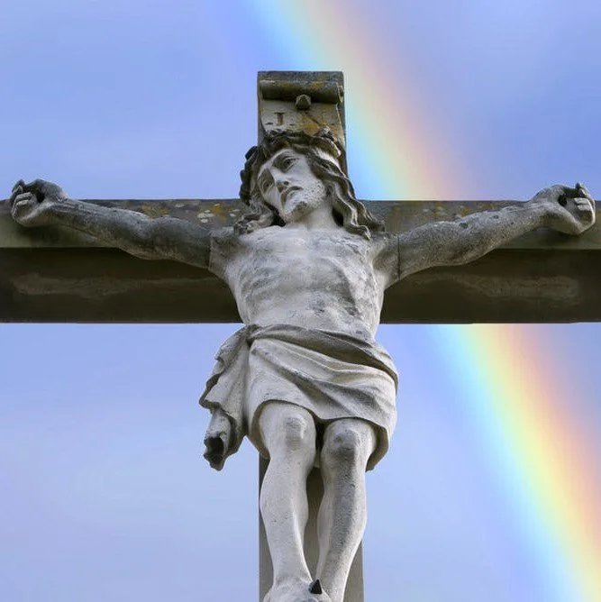 A stone crucifix pictured against a blue sky with a rainbow in the background