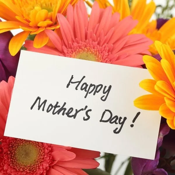A bunch of flowers with a hand-written greeting card saying ‘Happy Mother’s Day’