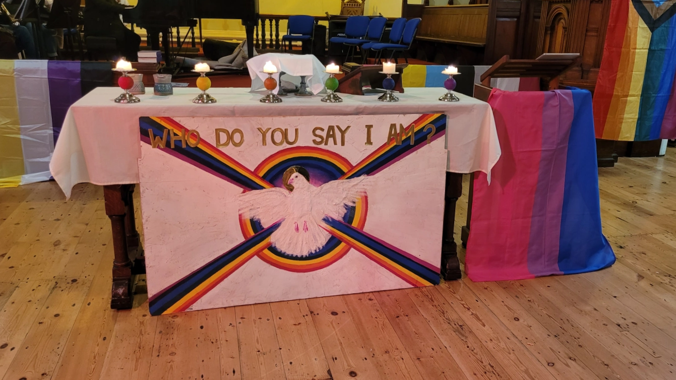  An original altar frontal artwork designed by Buddhist artist Tony O’ Connell for the first Open Table community in Liverpool. When Poppy chose to preach on this Gospel reading, she didn’t know that this would be at the front of the communion table during the service. The celebration marked the start of Bisexual Awareness Week - The bisexual flag (with blue, purple and pink stripes, is draped around the lectern from where Poppy preached. PHOTO: Poppy Thorpe. 