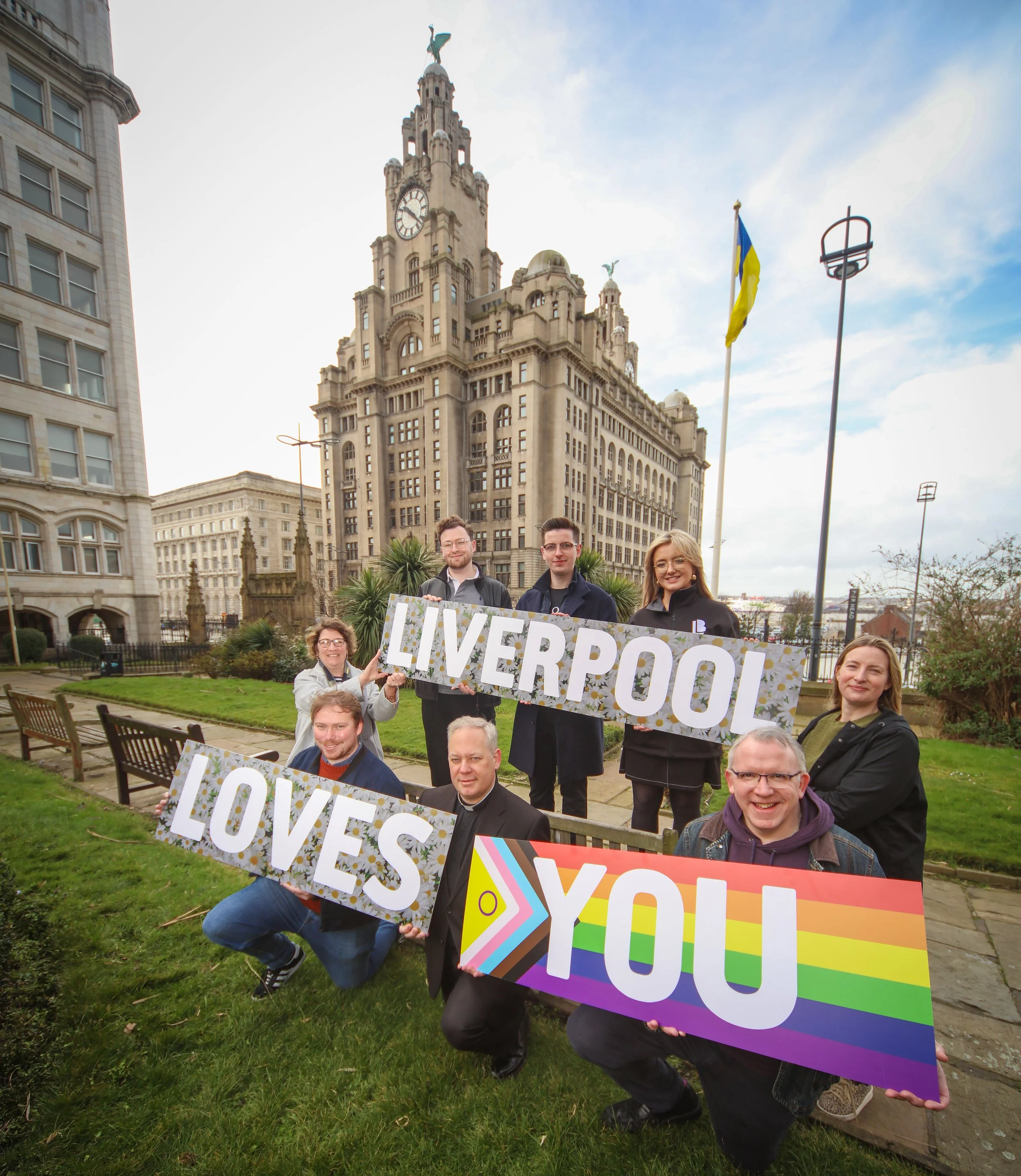 Members of the ‘Liverpool Loves You’ partnership hold signs saying ‘Liverpool Loves You’ in front of the city’s iconic Liver Building. PHOTO: Matt Goodfellow