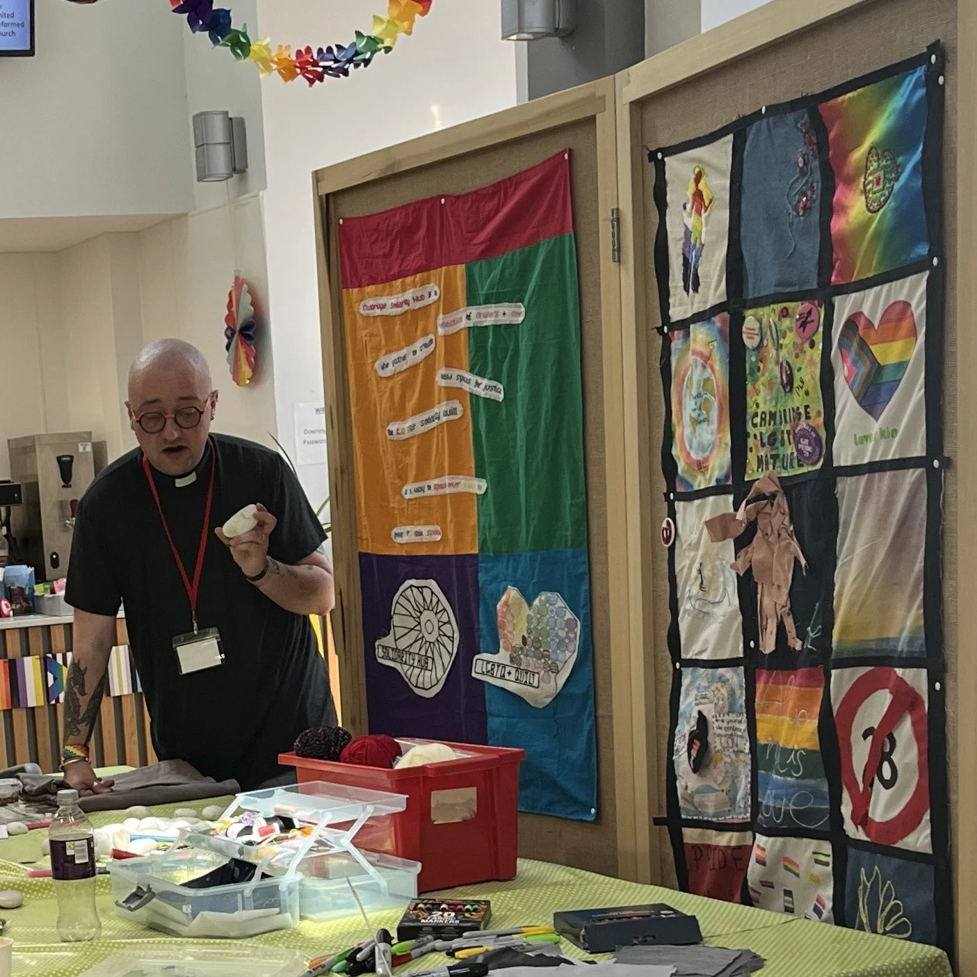  Alex hosting the craftivism workshop at the Open Table national gathering, with the Cambridge Solidarity Hub quilt on the display board. 