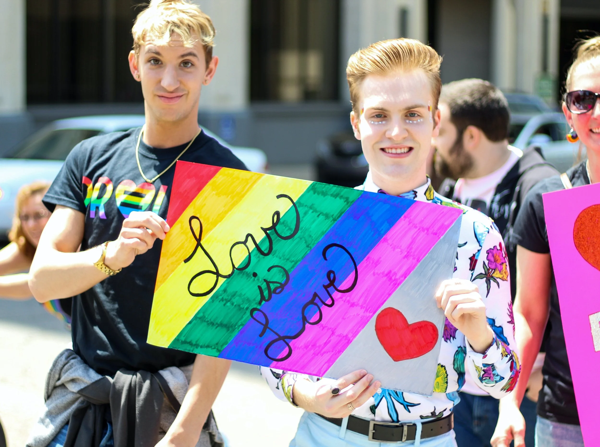  Three men holding a multicolour painted ‘Love Is Love’ banner. Photo by  Rosemary Ketchum . 