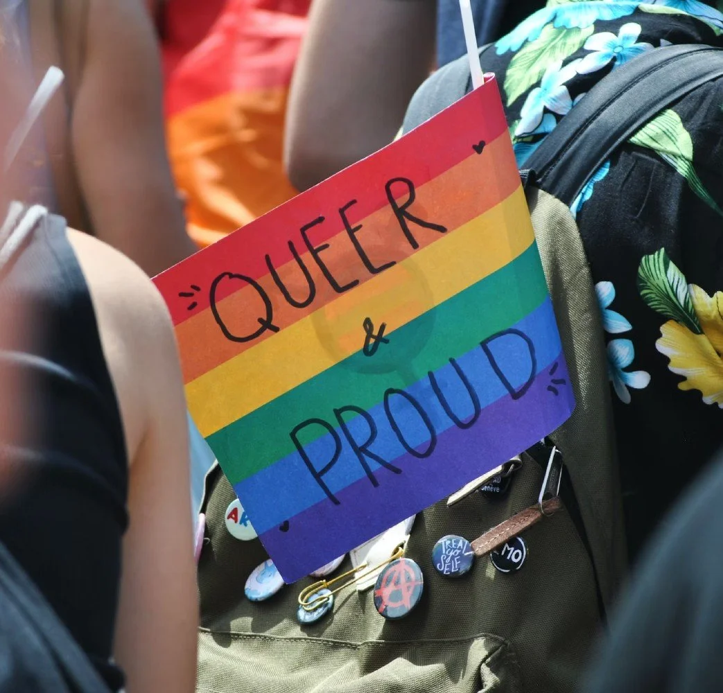  A rainbow flag with the words ‘Queer & Proud’ on the backpack of a person in a Pride march 