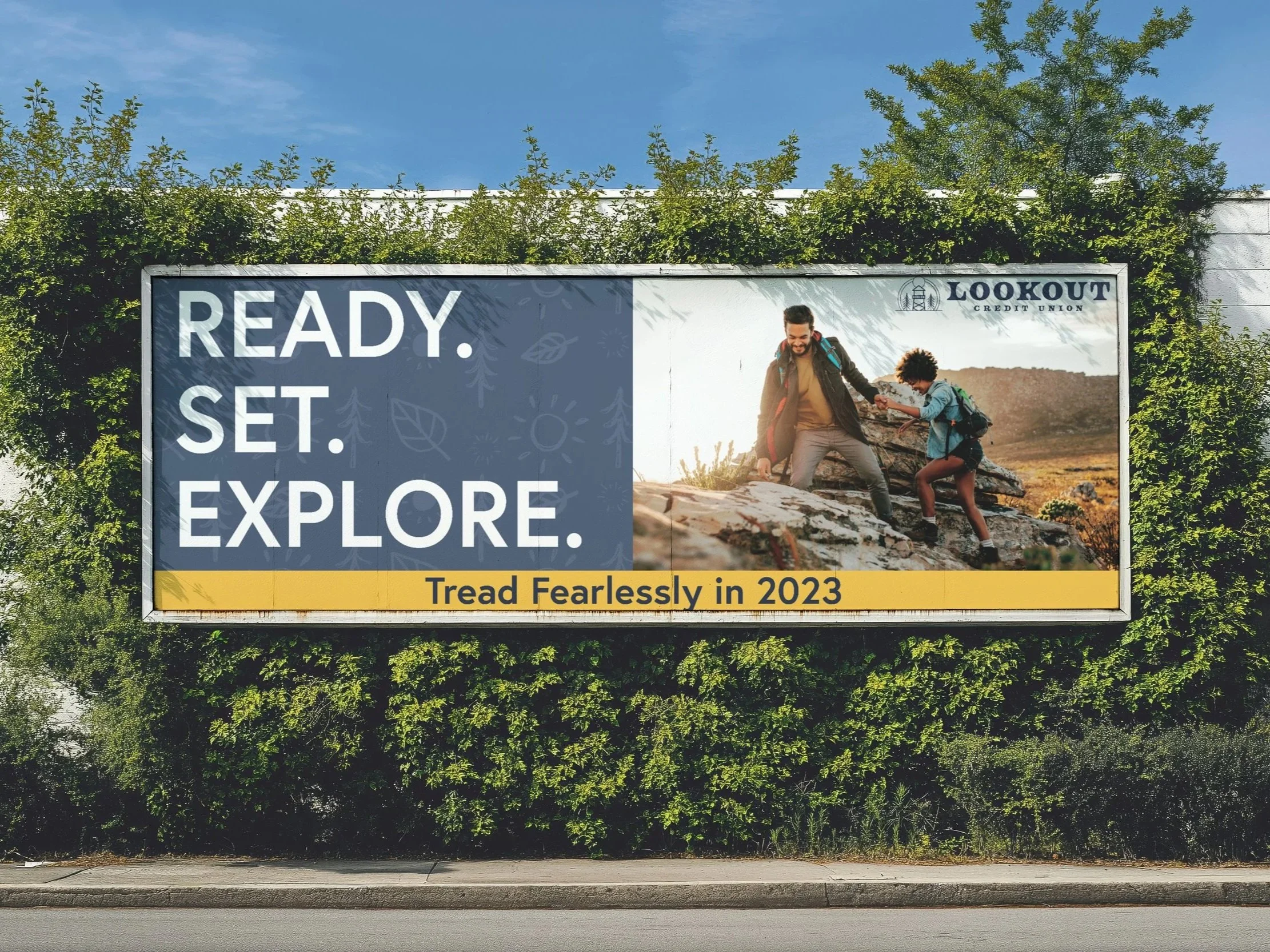 Billboard with the words 'READY. SET. EXPLORE.' and a photo of an adult helping a child climb a rocky hill outdoors, with trees and blue sky in the background.
