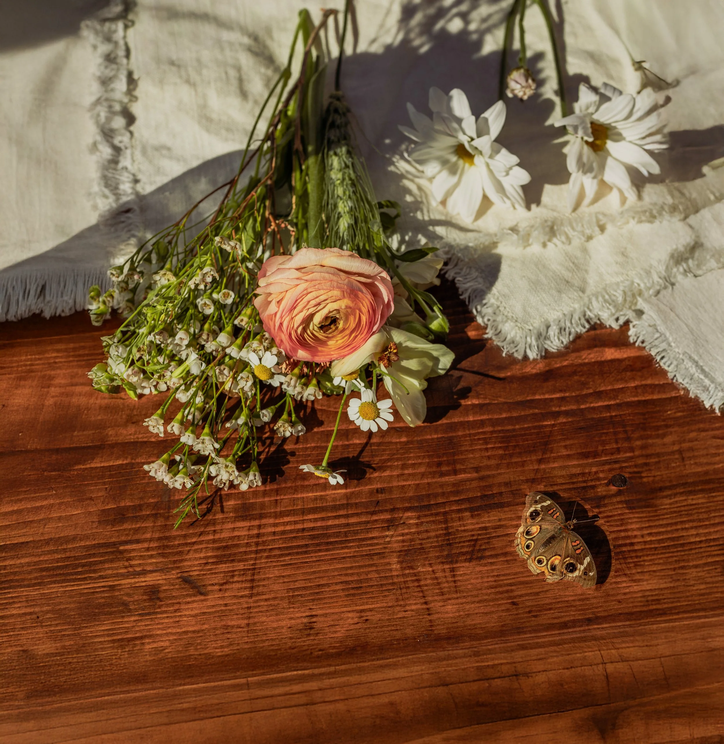 Wildflower bouquet and peach rose styled on wooden table in golden afternoon light.