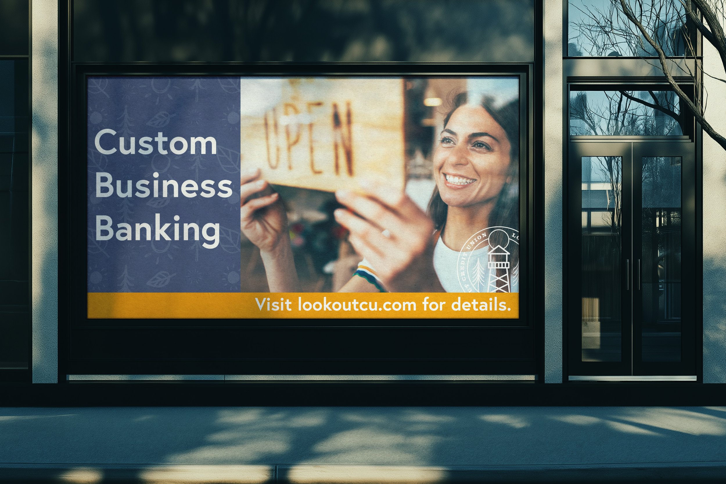A storefront window with an advertisement for custom business banking. The ad features a smiling woman putting an 'OPEN' sign on the window and includes text directing viewers to visit lookoutcu.com for more information.