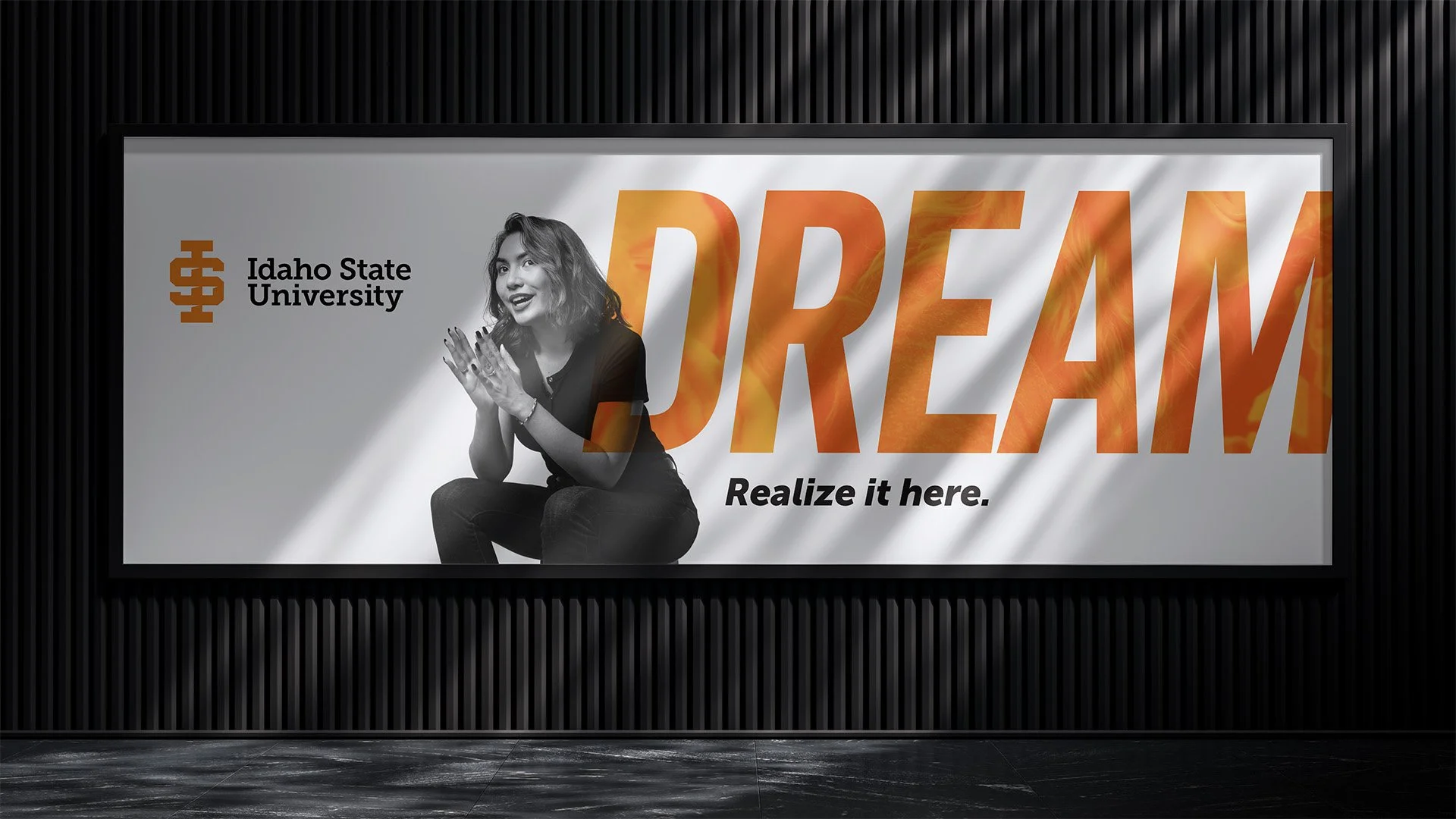 Billboard advertisement for Idaho State University featuring a black and white photo of a woman smiling, with large orange text spelling 'DREAM' and the phrase 'Realize it here.' underneath.
