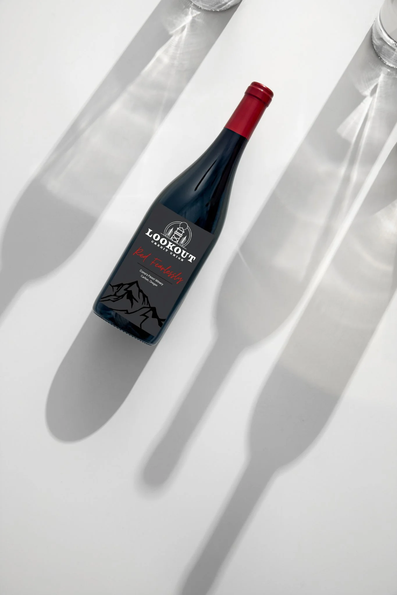 A bottle of red wine labeled 'Lookout Cabernet Union' with a red cap, placed on a white surface with shadows and reflections from nearby glass bottles.