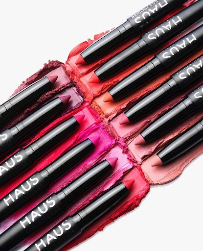 Lip crayons in various shades of red, pink, and nude laid on lipstick swatches.