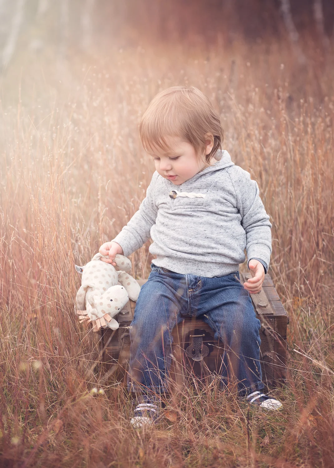 One year old boy playing with his favorite stuffie in the fall grass in Birds Hill Park.
