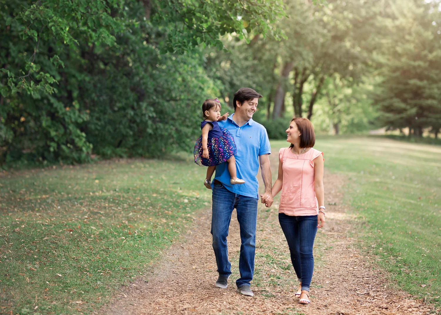 Family of three walking down a wood chip path in summer in Kings Park in Winnipeg.