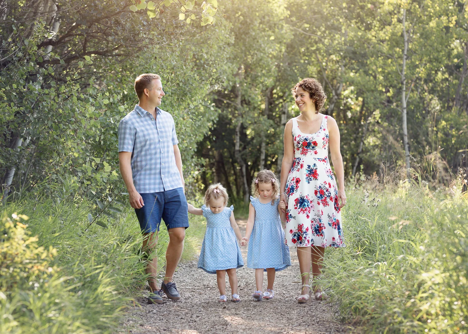 Young family of four laughing while walking down path in Assinboine Forest in Winnipeg.