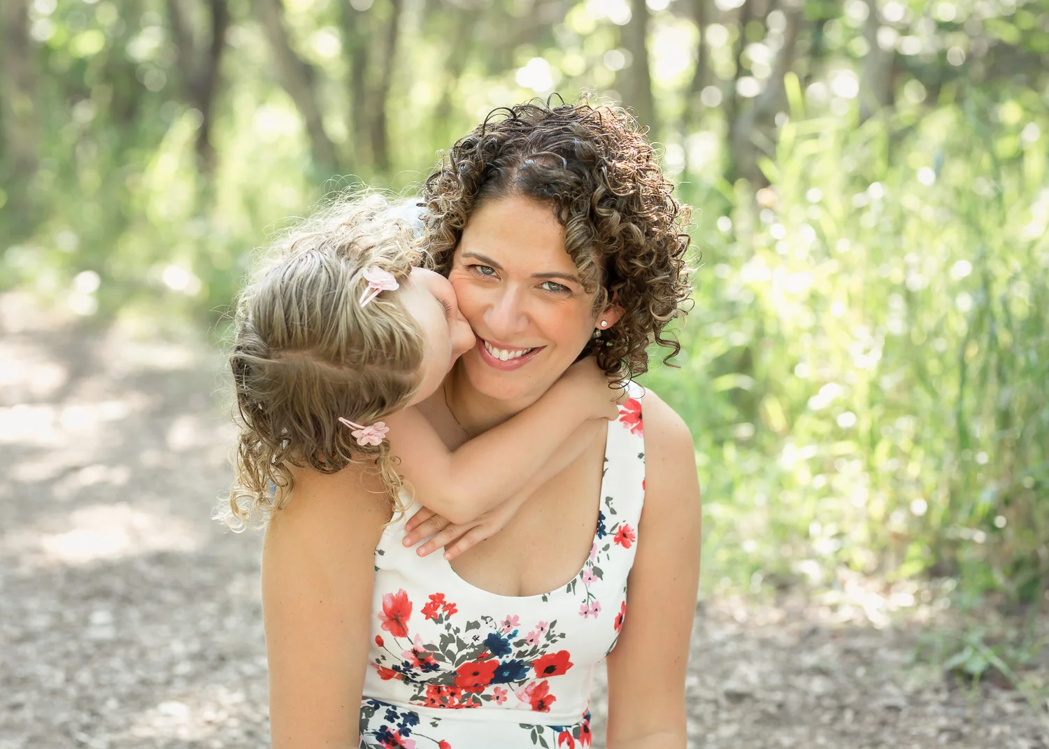 Mother smiling as daughter gives her hug in the forest during a family photoshoot in Winnipeg.