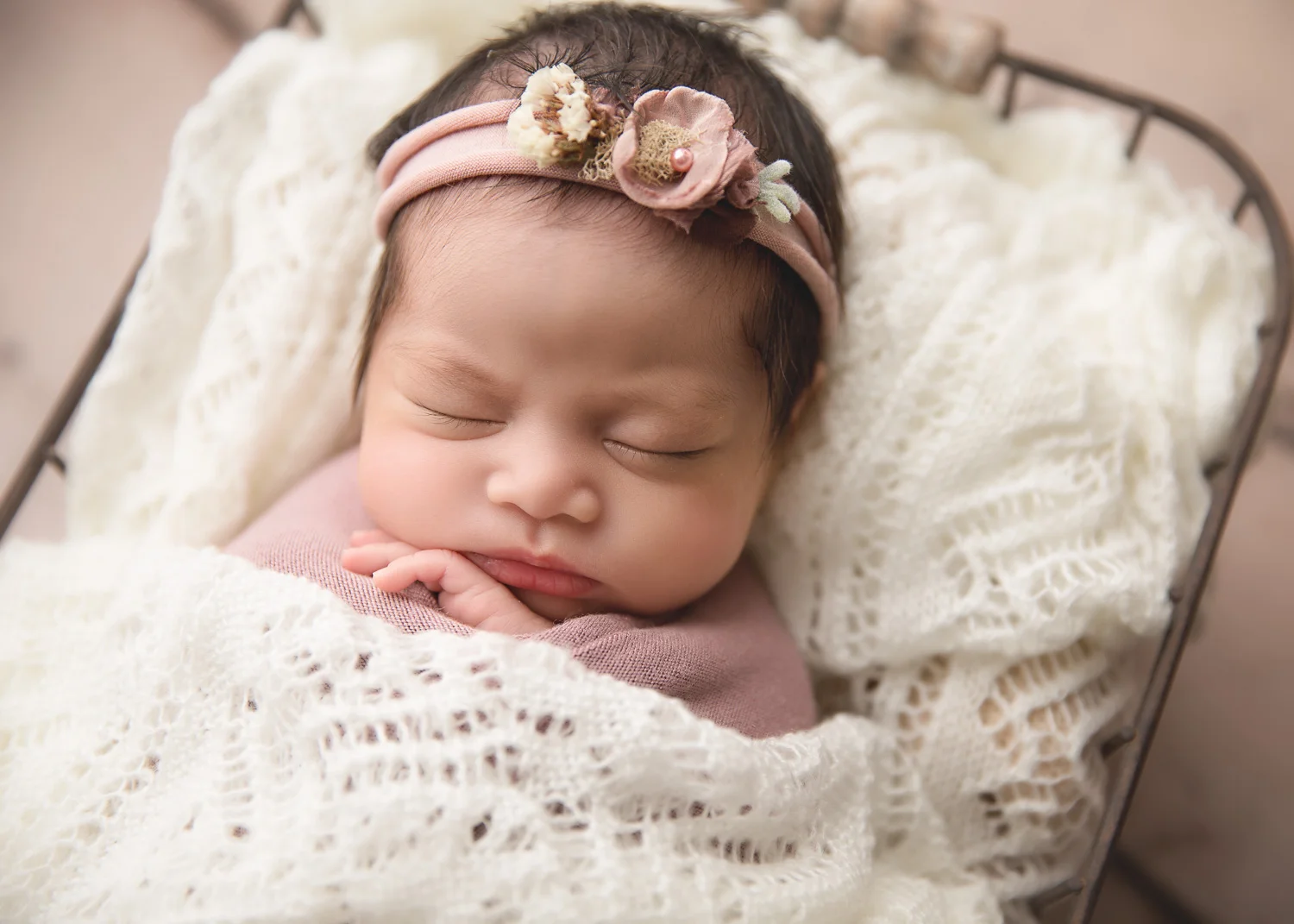 Baby girl sleeping under cream knit blanket in a basket for newborn photo session in Winnipeg.