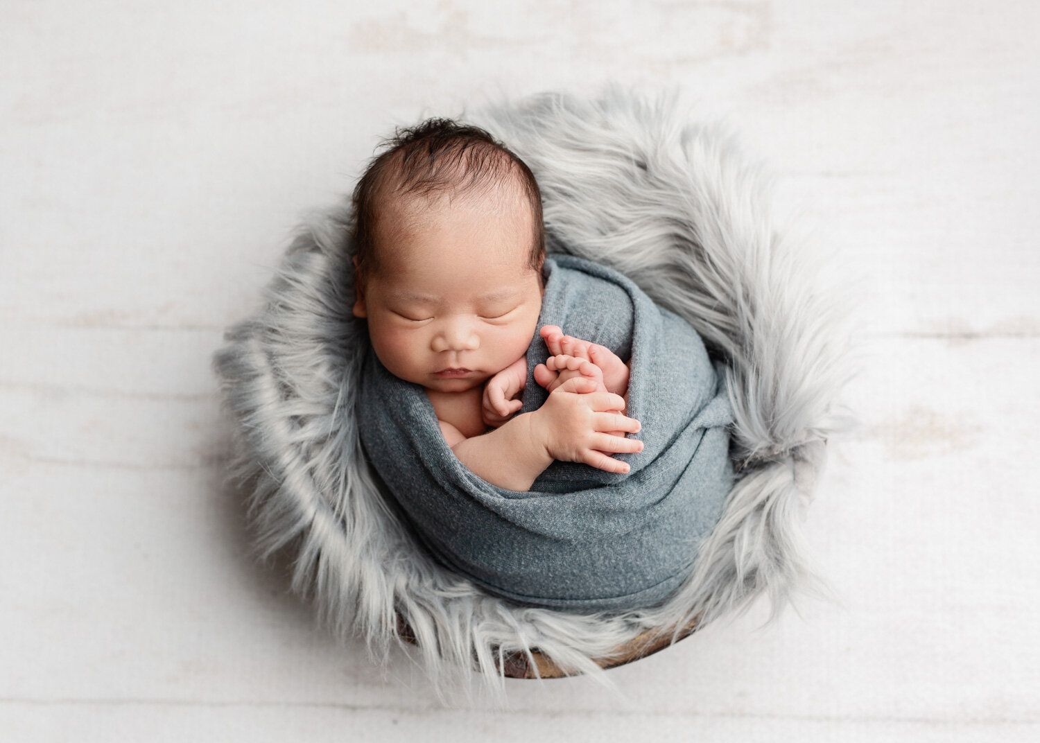  newborn baby boy wrapped in grey with fluffy grey wool in bowl prop in Winnipeg photography studio session 