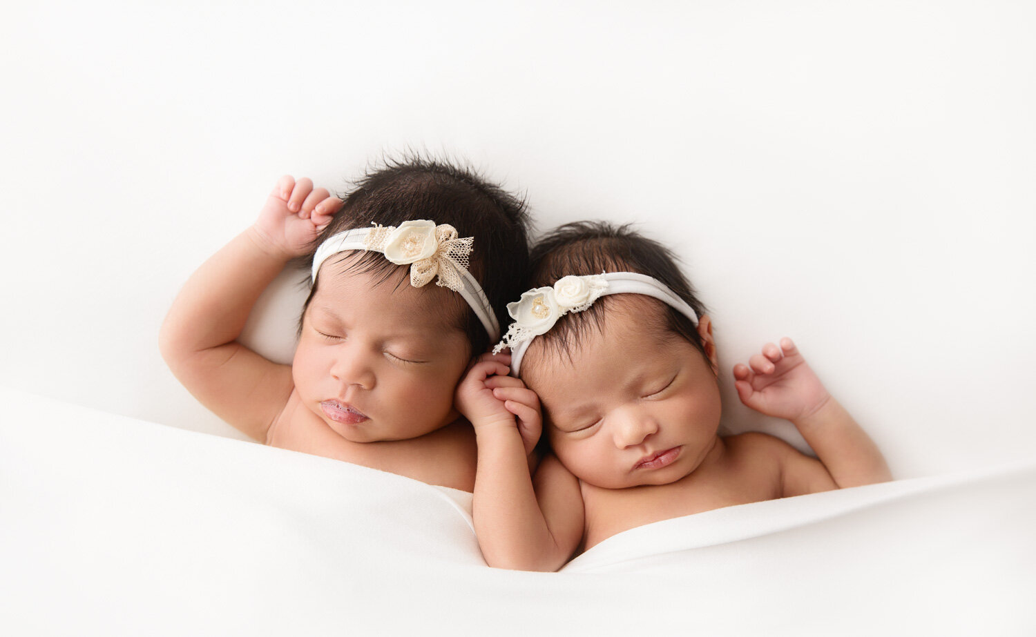  Beautiful newborn baby girl twins holding hands on classic white backdrop during photosession in Winnipeg 