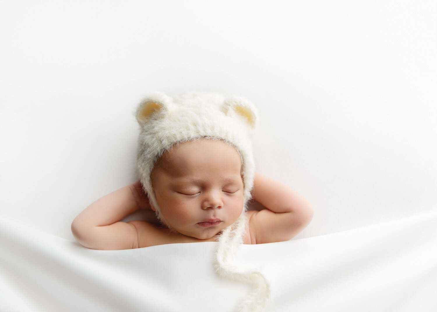  Classic white set up with baby boys hands tucked behind head with cozy bear hat with Sue Skrabek Photography in WInnipeg 