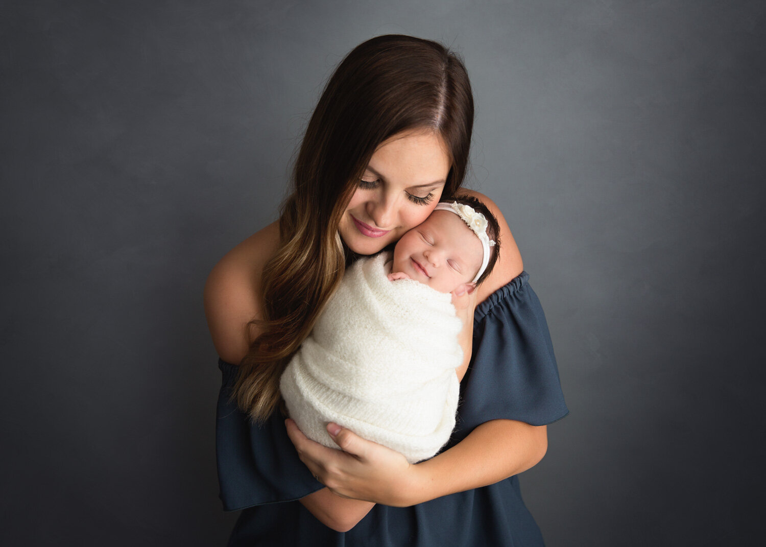  baby girl wrapped in white smiling with mom holding her during newborn photoshoot in Winnipeg 