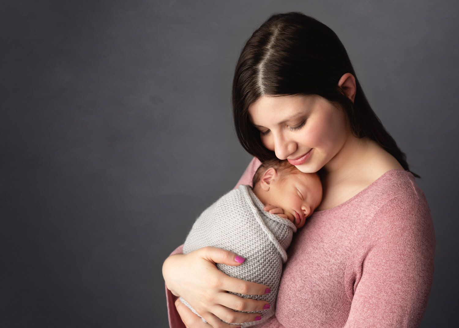  Smiling mother cuddling newborn baby boy wrapped sweetly in arms in Winnipeg with Sue Skrabek 