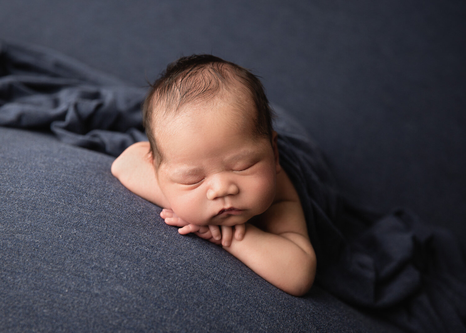  Chubby cheeks baby boy resting chin on hands on blue blanket in Winnipeg newborn studio 