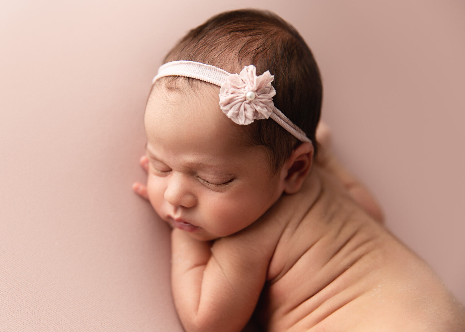  Newborn baby girl back rolls on bluh pink with matching headband in Winnipeg photography studio 