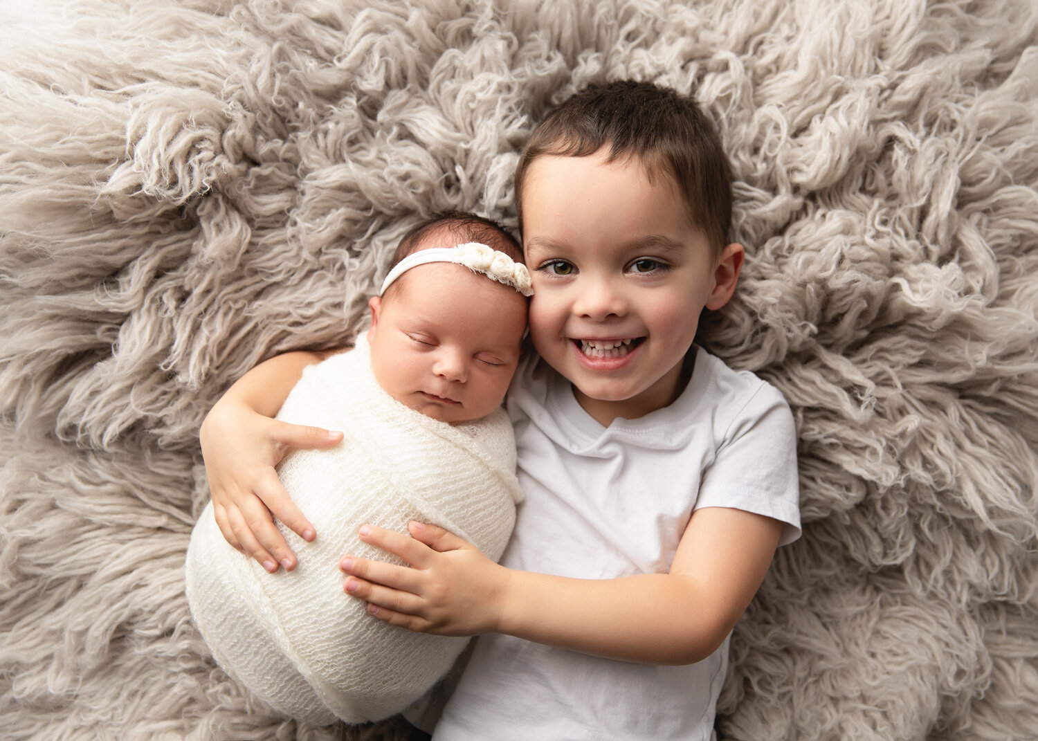  Proud brother holding baby sister during Sue Skrabek Photography newborn session in Winnipeg on flokati rug 