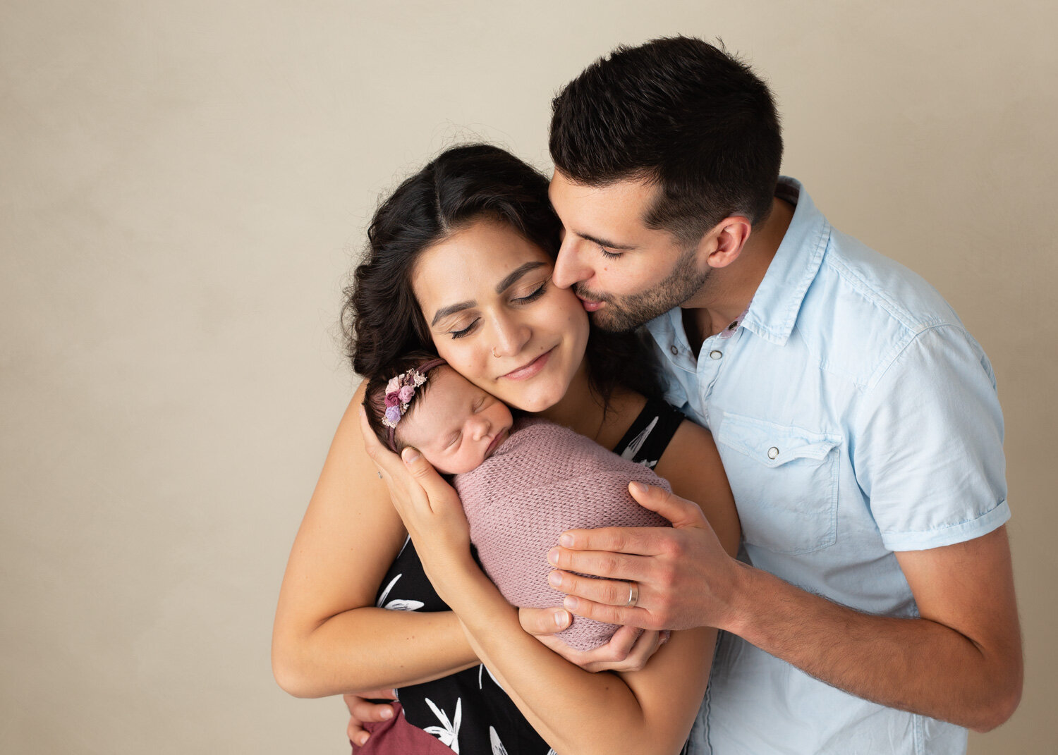  New parents lovingly holding newborn baby girl wrapped in dusty rose during photosession in Winnipeg 